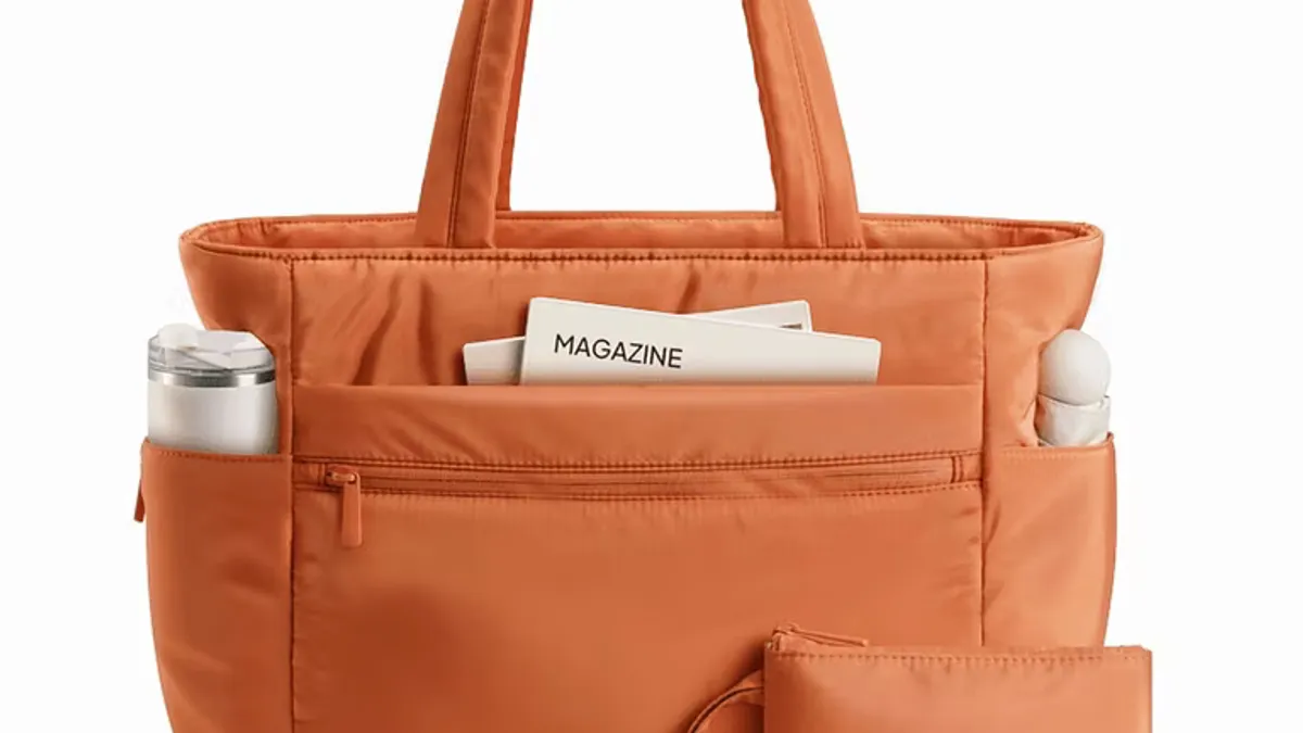 Orange laptop tote bag with front pockets, a magazine, and a pouch